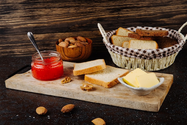 Вид сбоку банку с красной икрой с маслом из белого и ржаного хлеба, миндаля и грецкого ореха на доске