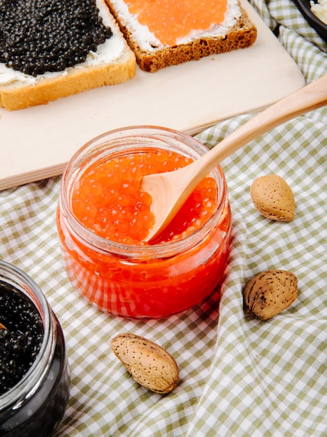 Foto gratuita vista laterale barattolo di caviale rosso con cucchiaio di legno di mandorle e caviale toast sul tavolo