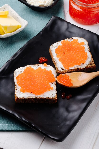 Side view red caviar toast rye bread with cottage cheese red caviar and butter on the table