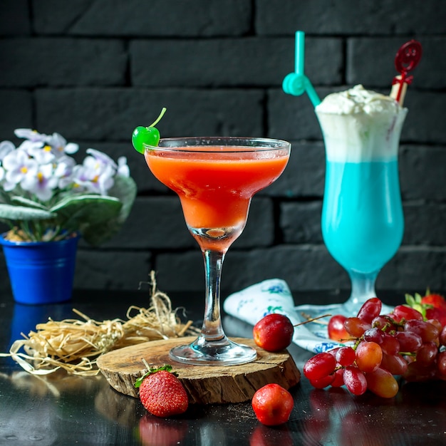 Side view of red cocktail in glass with fresh fruits on wooden table