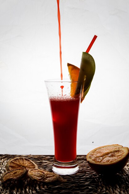 Side view red fruit smoothie with tubules for beverages and dried lemon and drops in serving napkins