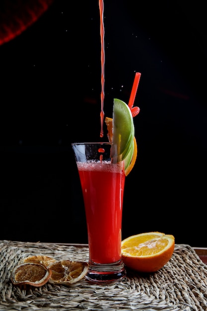 飲料用の細管と半分オレンジ色のナプキンのサービングの滴と赤い果実のスムージーの側面図