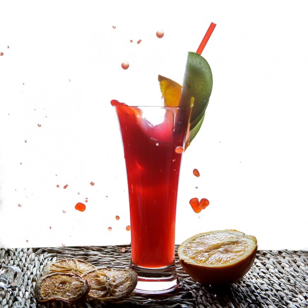 Side view red fruit smoothie with tubules for beverages and half orange and drops in serving napkins