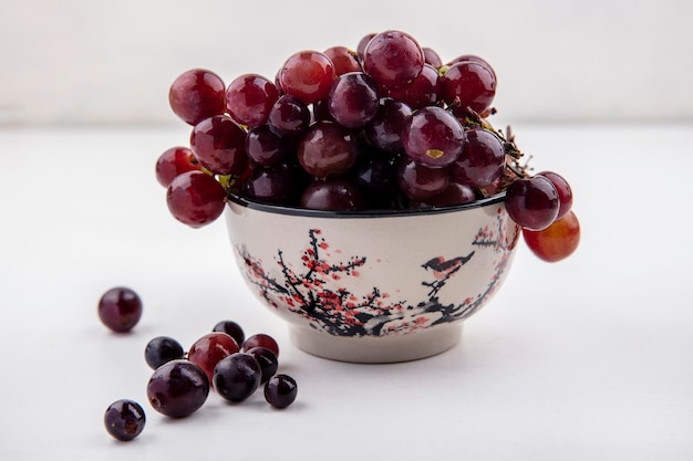 Side view of red grape in bowl and on white background