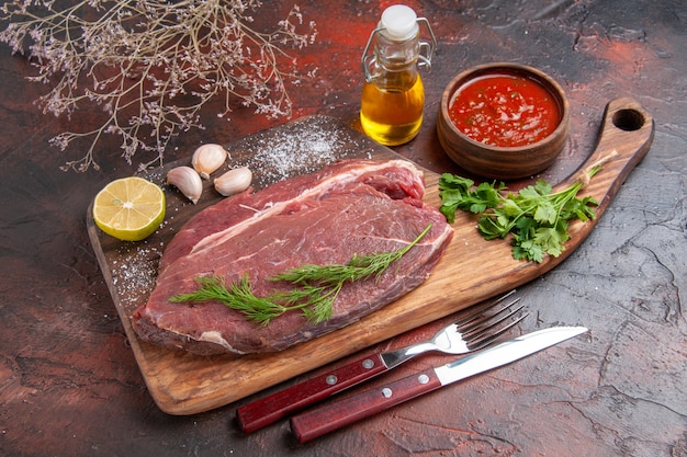 Side view of red meat on wooden cutting board and garlic green oil bottle lemon ketchup on dark background