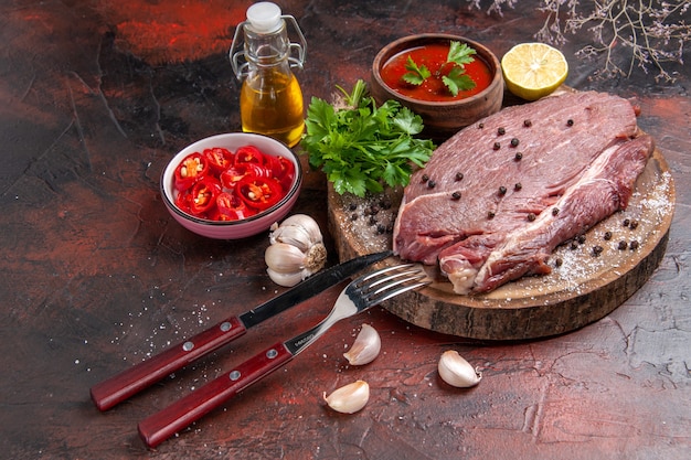 Side view of red meat on wooden tray and garlic green ketchup and chopped pepper oil bottle lemon on dark background