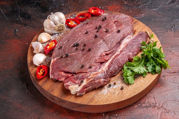 Side view of red meat on wooden tray and garlic green lemon onion on dark background