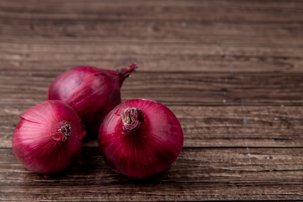 Side view of red onions on left side and wooden background with copy space