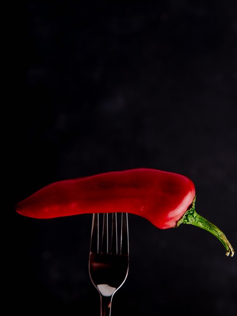 Side view of red pepper on fork on black background with copy space