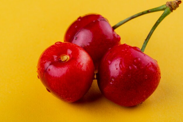 Side view of red ripe cherries with water drops isolated on yellow