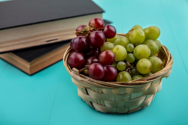 Vista laterale della merce nel cestino dell'uva rossa e bianca con i libri chiusi su priorità bassa blu