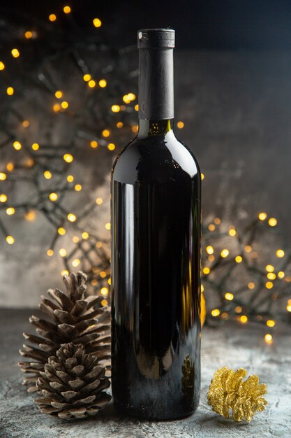 Side view of red wine bottle for celebration and two conifer cones on dark background