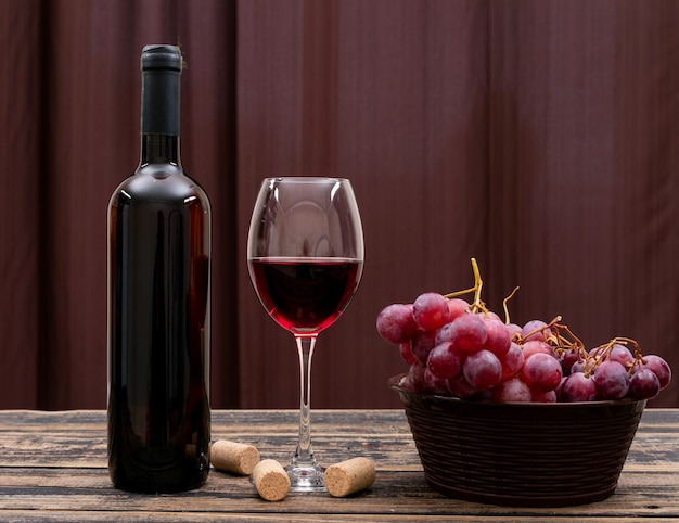 Side view red wine in bottle, glass and grape on dark table and horizontal