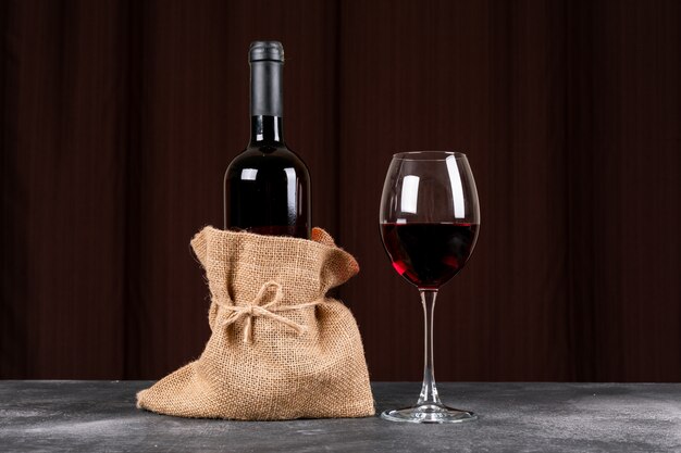 Side view red wine bottle in sackcloth bag on dark table and horizontal