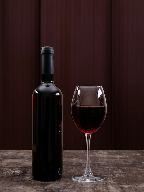 Вид сбоку красное вино в бутылке с бокалом на вертикали