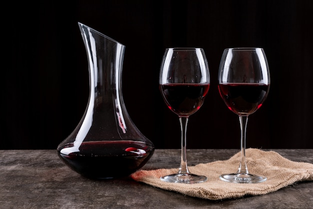 Вид сбоку красное вино в очках и льняной тканью на темной горизонтали