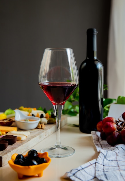 Вид сбоку красного вина с различными видами сыра, оливкового, грецкого ореха, винограда на белом фоне