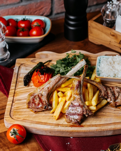 Side view of ribs kebab with french fries rice and vegetables on a wooden board