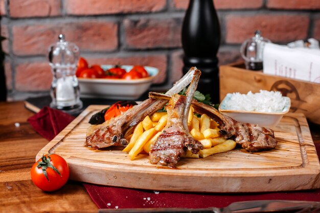 Side view of ribs kebab with french fries rice and vegetables on a wooden board