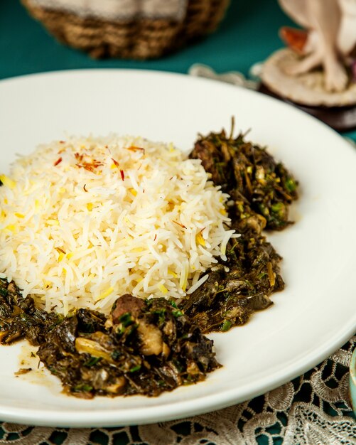 Side view of rice with stewed meat and herbs in white plate