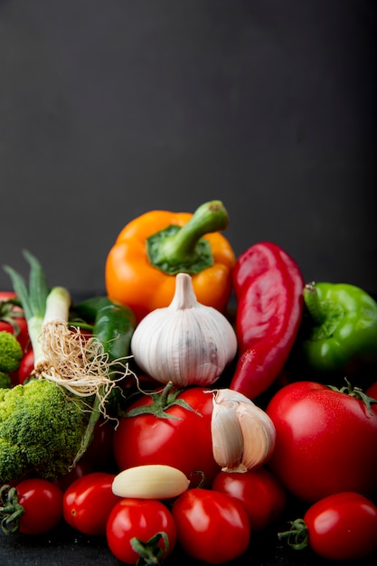 Side view of ripe fresh vegetables colorful bell peppers tomatoes garlic broccoli and green onion on black background