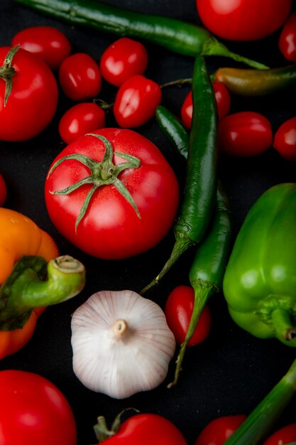 Side view of ripe fresh vegetables colorful bell peppers tomatoes garlic broccoli and green onion on black background