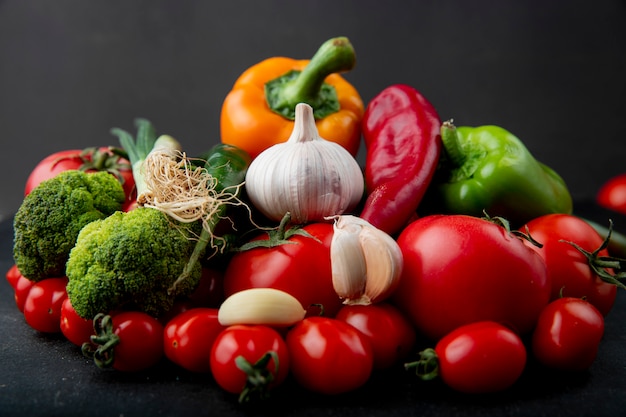 Side view of ripe fresh vegetables colorful bell peppers tomatoes garlic broccoli and green onion on black background