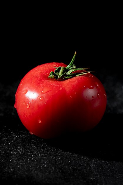 Side view of ripe wet tomato on black background