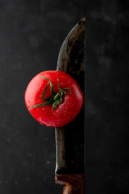 黒の背景でナイフで熟したウェットトマトの側面図