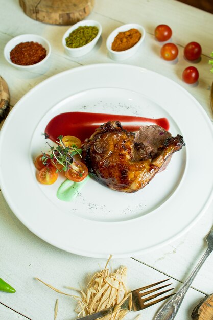 Side view of roast chicken leg with cherry tomatoes and ketchup on white plate
