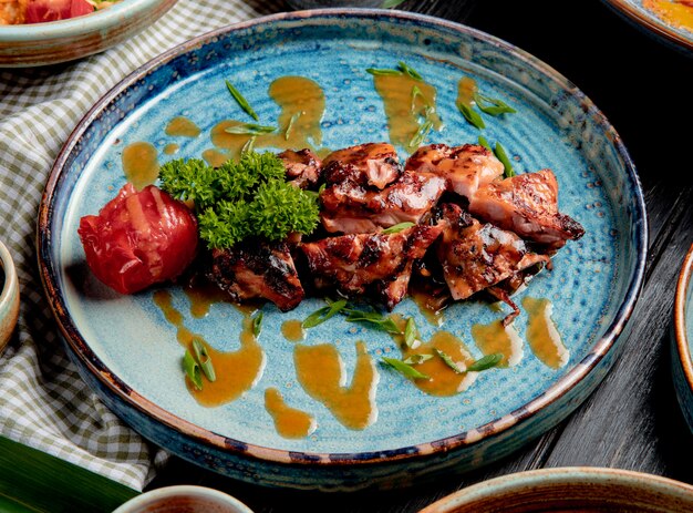 Side view of roasted chicken with grilled tomato fresh herbs and sauce on a plate on wood
