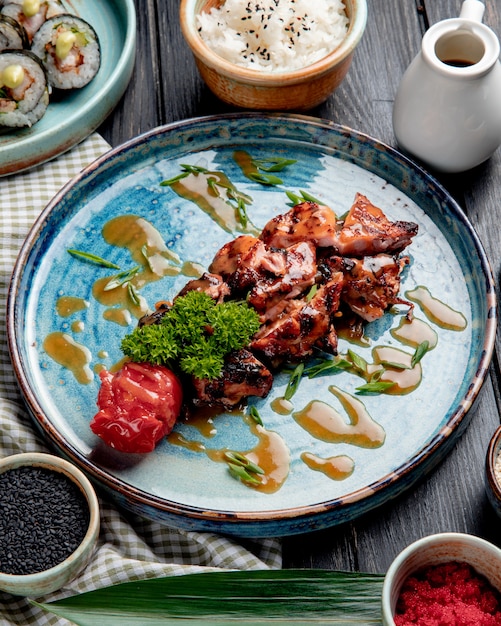 Side view of roasted chicken with grilled tomato fresh herbs and sauce on a plate on wood