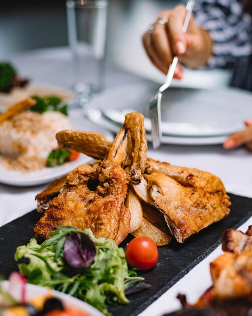 Side view of roasted chicken with herbs and cherry tomato on a black board