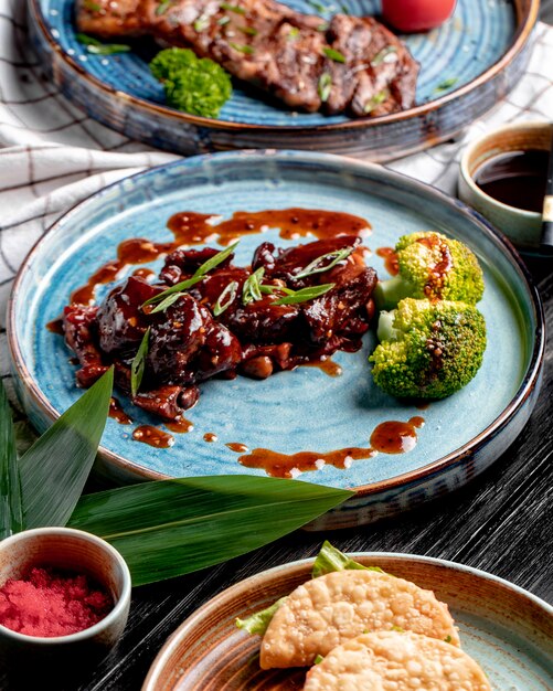 Side view of roasted chicken with sweet and sour sauce and broccoli on a plate on plaid tablecloth