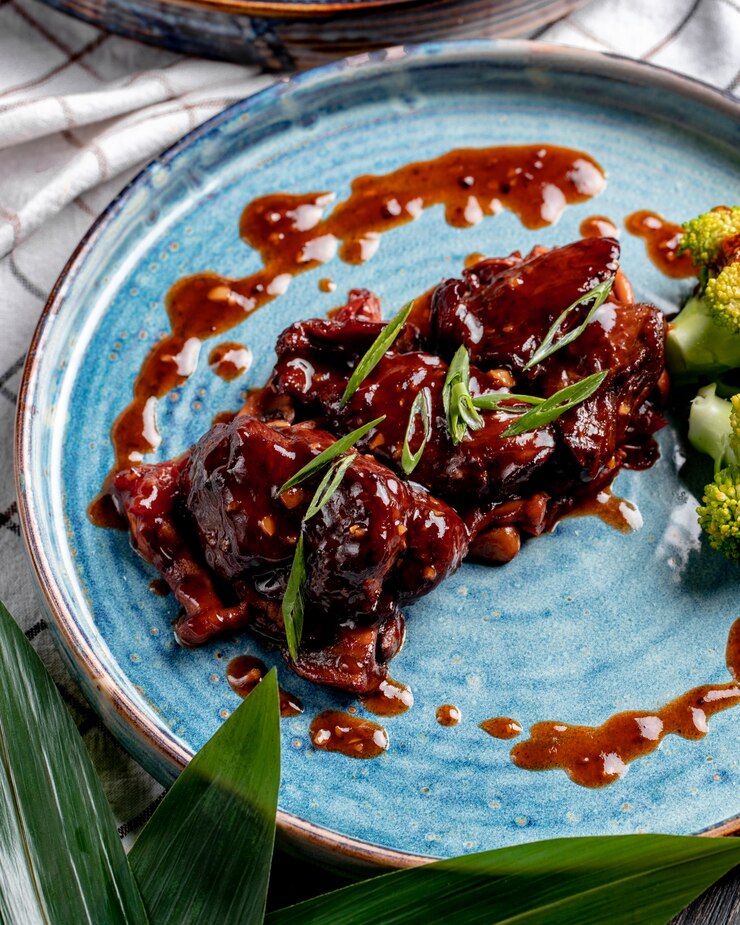 Free Photo side view of roasted chicken with sweet and sour sauce and broccoli on a plate on plaid tablecloth
