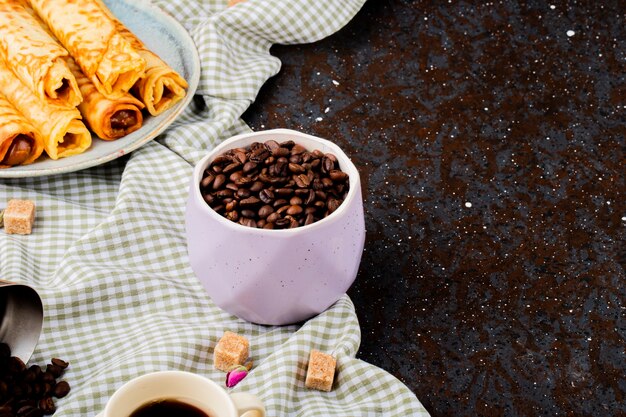 Side view of roasted coffee beans in a bowl and wafer rolls with condensed milk on a plate with copy space