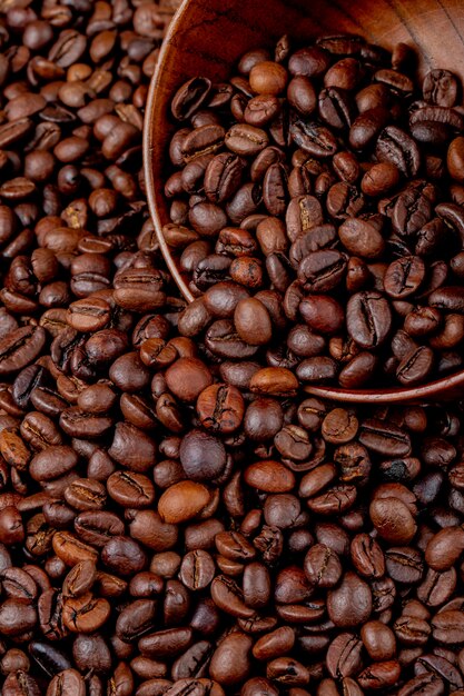 Side view of roasted coffee beans scattered from wooden bowl on coffee beans