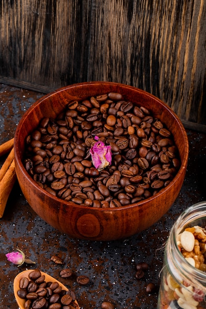 Side view of roasted coffee beans in a wooden bowl on black background