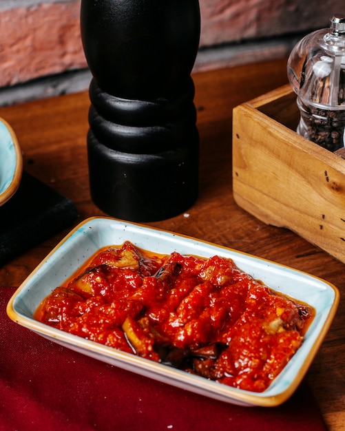 Side view of roasted eggplant pieces with spicy tomato sauce and olive oil on a wooden table