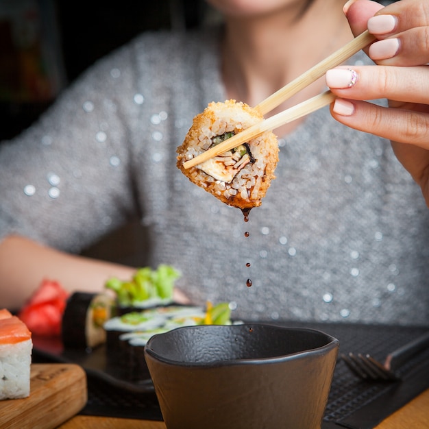 Side view roll with soy sauce and chopstick in woman hand