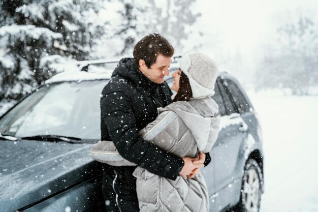 Side view of romantic couple kissing in the snow while on a road trip