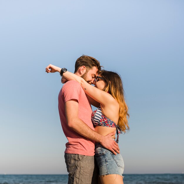 Side view of romantic young couple standing against blue sky at beach