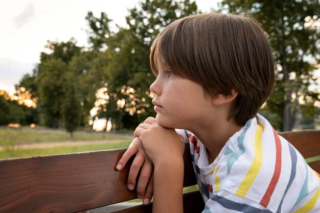 Вид сбоку грустный мальчик на скамейке