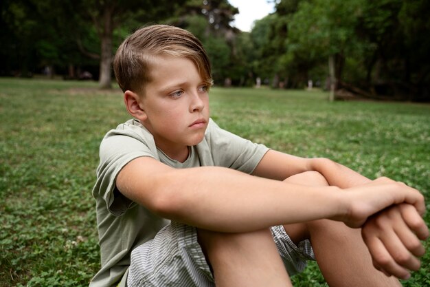 Side view sad boy sitting on grass