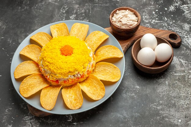 Side view of salad over the plate stand with cheese and bowl of eggs on side on dark grey background