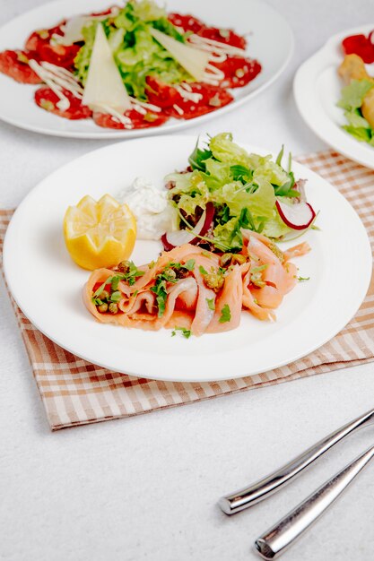 Side view of salmon carpaccio with lemon and fresh salad on the table