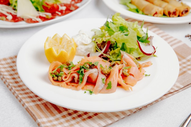 Side view of salmon carpaccio with lemon and fresh salad