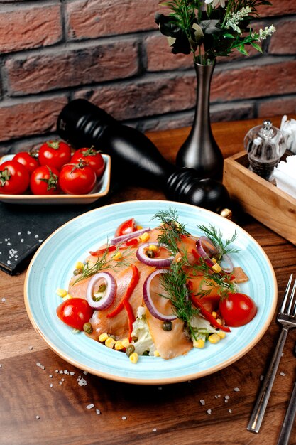 Side view of salmon salad with red onions cabbage and corns topped with dill in plate on wooden table