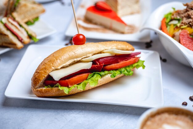 Side view sandwich white bread with smoked sausage cheese sliced tomato and lettuce on a plate