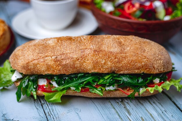 Side view sandwich with tomato mozzarella cheese and arugula on the table